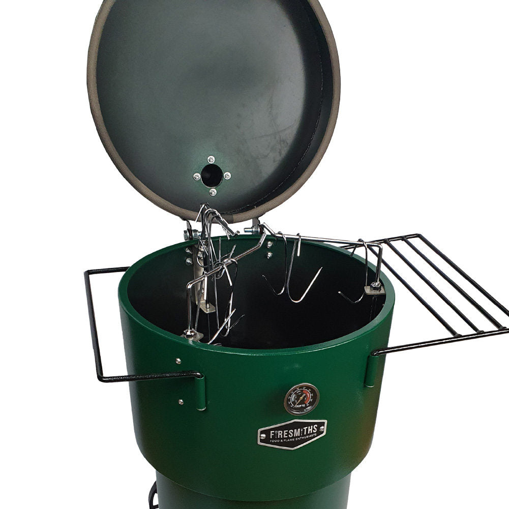 Close-up of the Firesmiths Hero Smoker & Grill in a forest green finish with the lid open, showcasing the stainless steel hanging rack system, meat hooks, dual side shelves, and built-in temperature gauge for versatile smoking.