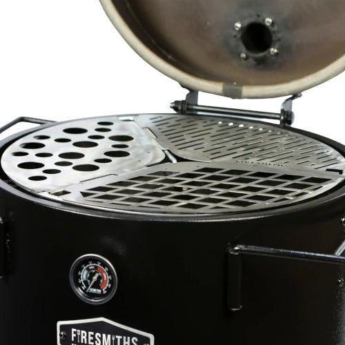 Close-up of the Firesmiths Hero Smoker with the lid open, featuring the modular stainless steel cooking grate system with interchangeable grill, searing, and accessory inserts for versatile wood-fired cooking.