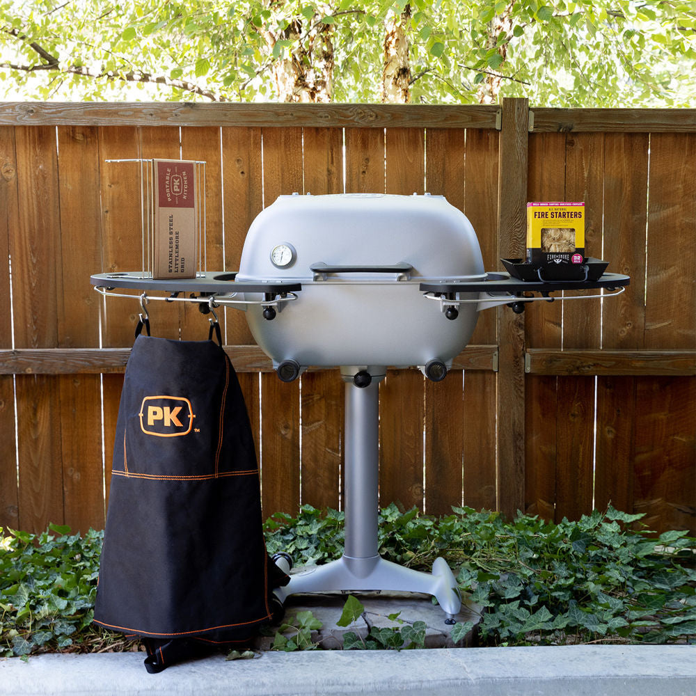 Firesmiths PK Series charcoal grill displayed in a backyard with a premium apron, fire starters, grilling accessories, and side shelves, ready for an authentic outdoor barbecue experience.