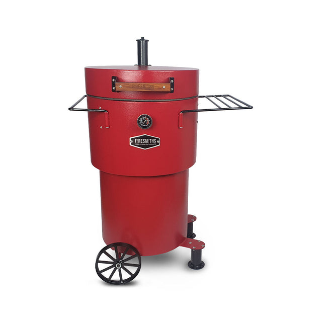 A red vertical charcoal smoker and grill with two side shelves and wheels for mobility. 