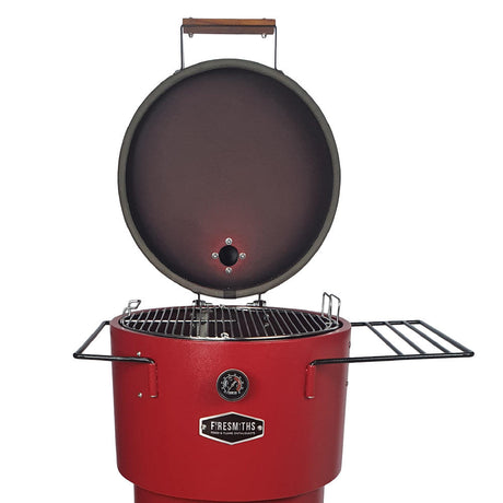 A red vertical charcoal smoker and grill with two side shelves and wheels for mobility. 