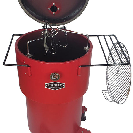 A red vertical charcoal smoker and grill with two side shelves and wheels for mobility.