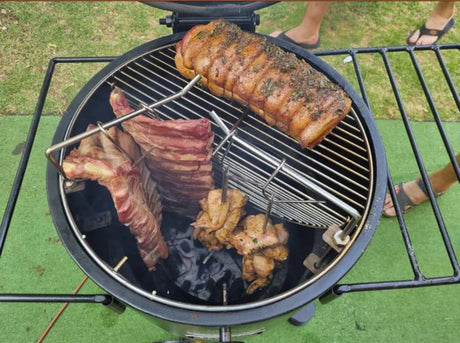 Firesmiths Hero Smoker & Grill in use with pork belly roasting on the cooking grate while ribs and chicken hang below, showcasing the versatile combination grilling and wood-fired smoking system.