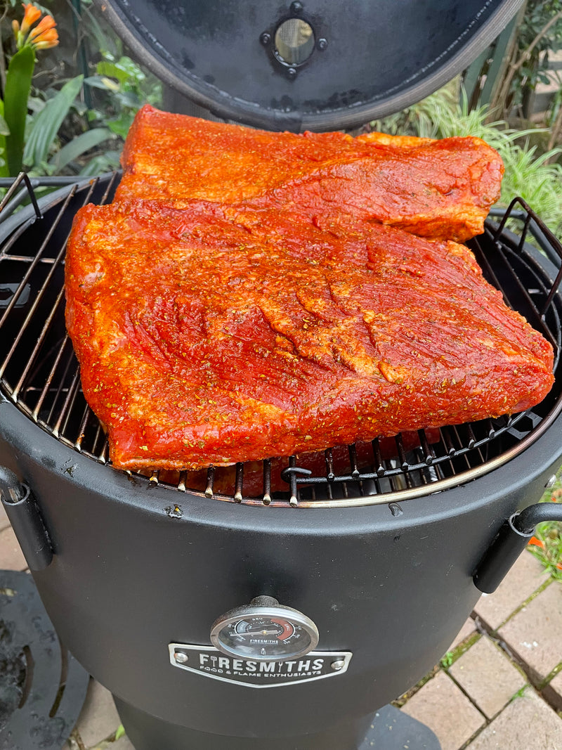 Large seasoned briskets smoking on the cooking grate of a Firesmiths Hero Smoker & Grill with the lid open, showcasing low-and-slow wood-fired barbecue cooking for tender, flavourful results.