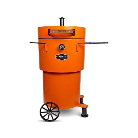 Firesmiths Hero Smoker & Grill in the Burnt Orange finish featuring a built-in temperature gauge, adjustable chimney, wooden handle, dual side shelves, and a wheeled base for premium wood-fired smoking and grilling.