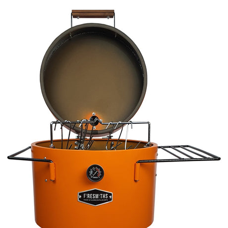Firesmiths Hero Smoker & Grill in the Burnt Orange finish with the lid open, showcasing the stainless steel hanging rack system, meat hooks, dual side shelves, and built-in temperature gauge for versatile wood-fired smoking.