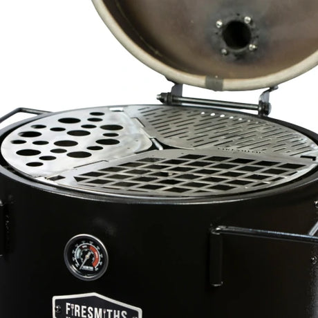 Close-up of the Firesmiths Hero Smoker with the lid open, featuring the modular stainless steel cooking grate system with interchangeable grill, searing, and accessory inserts for versatile wood-fired cooking.