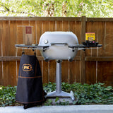 Firesmiths PK Series charcoal grill displayed in a backyard with a premium apron, fire starters, grilling accessories, and side shelves, ready for an authentic outdoor barbecue experience.