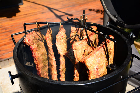 Stainless steel smoking hook rack set holding thick cuts of meat inside a Firesmiths Hero Smoker & Grill, designed for hanging ribs, brisket, and other large cuts for even wood-fired smoking.